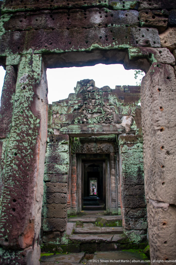 Multiple rectangular sandstone doorways aligned through roofless, lichen-covered temple chambers.