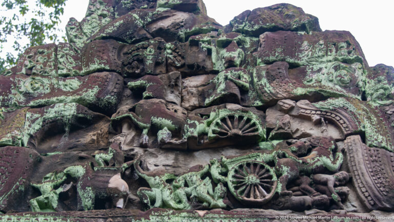 Lichen-covered sandstone pediment carved with figures, foliage, and circular ornamental motifs.