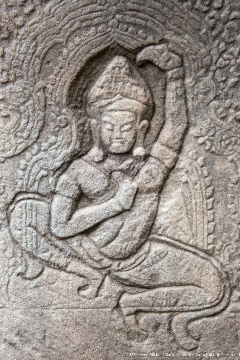 Weathered sandstone relief of a female figure reclining beneath a curved decorative frame.