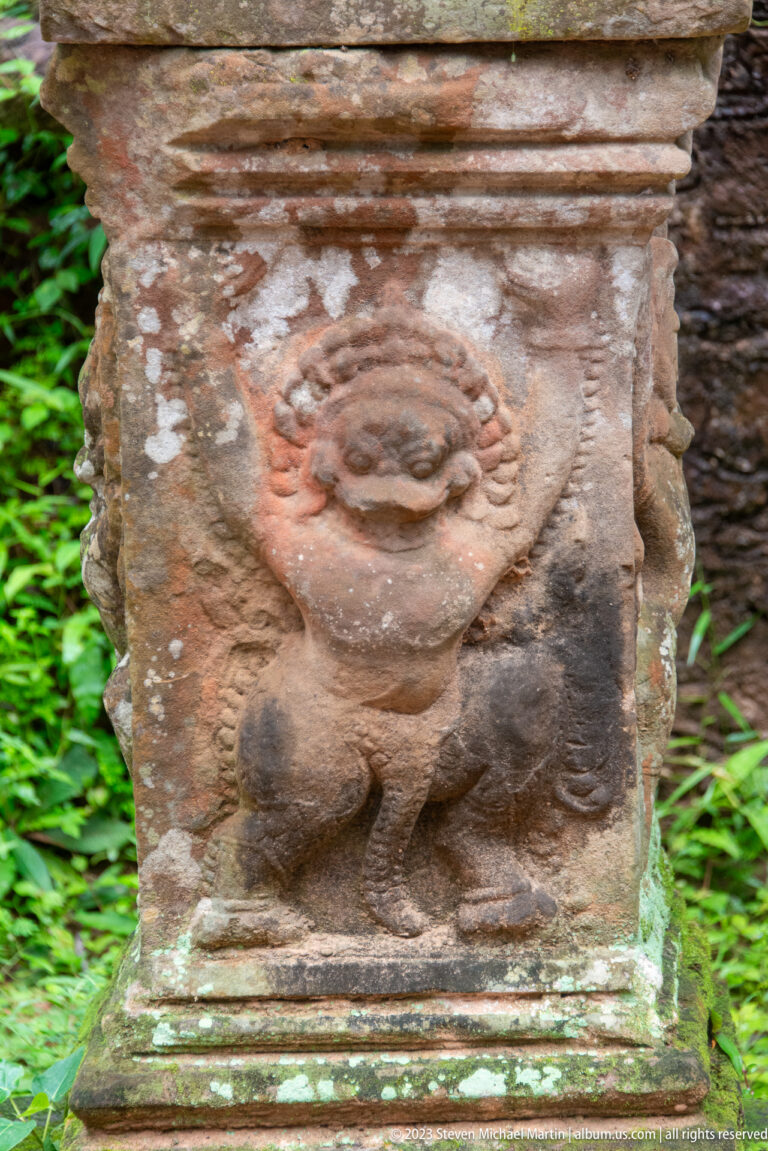 Eroded frontal guardian relief with a broad face and crouching body on a stone block.