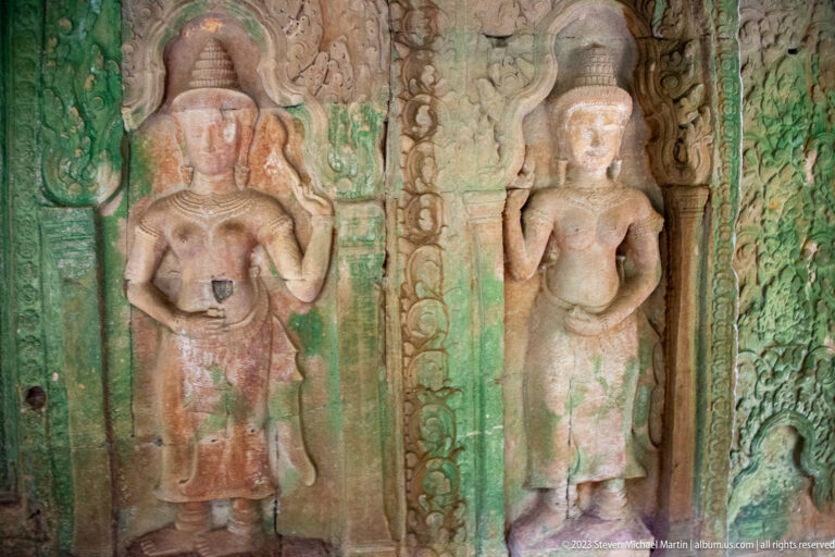 Two standing carved female deities with headdresses and jewelry on green-stained sandstone panels.
