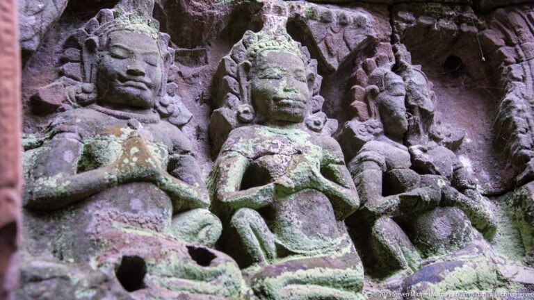 Cluster of weathered female stone figures with headdresses and folded hands in deep relief.