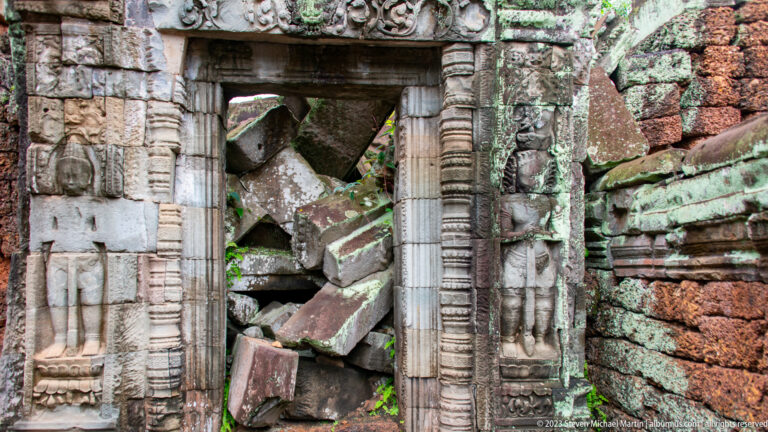 Carved sandstone doorway with female figures on the jambs and large fallen blocks behind it.