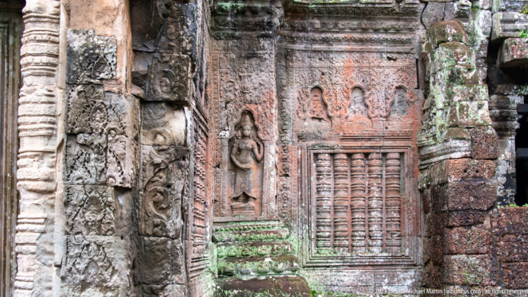 Ornate sandstone wall with female reliefs, carved borders, and a baluster-style window.