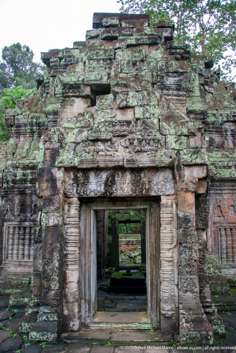 Weathered sandstone entrance in a partially collapsed façade with another doorway aligned beyond.