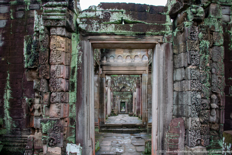 Long line of nested sandstone doorways receding through dark, lichen-covered temple chambers.