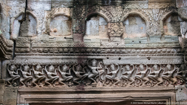 Sandstone relief with a central figure flanked by rows of small dancers beneath arched ornament.