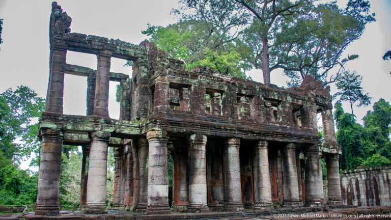Oblique view of a two-story sandstone building with tall columns below and open bays above.