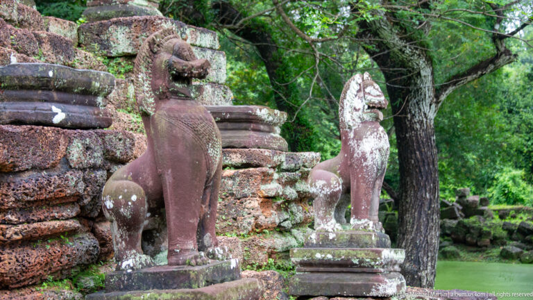 Two weathered sandstone lion guardians standing beside a temple approach under trees.