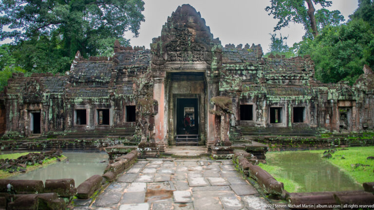 Stone causeway crossing green water toward a towered sandstone temple entrance.