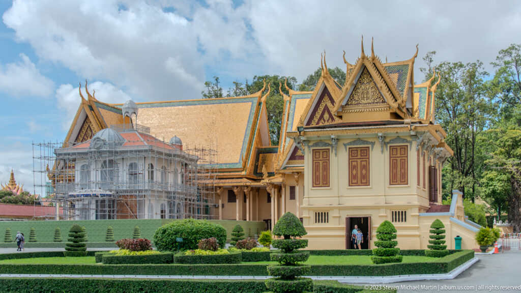 Multiple Royal Palace buildings around clipped hedges and lawns, with scaffolding on a larger hall in the background.