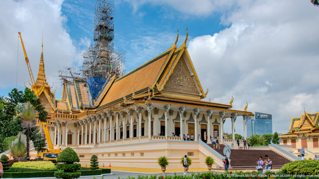 Oblique view of the Throne Hall with colonnade, gold-edged roofs, central spire, scaffolding, and visitors.