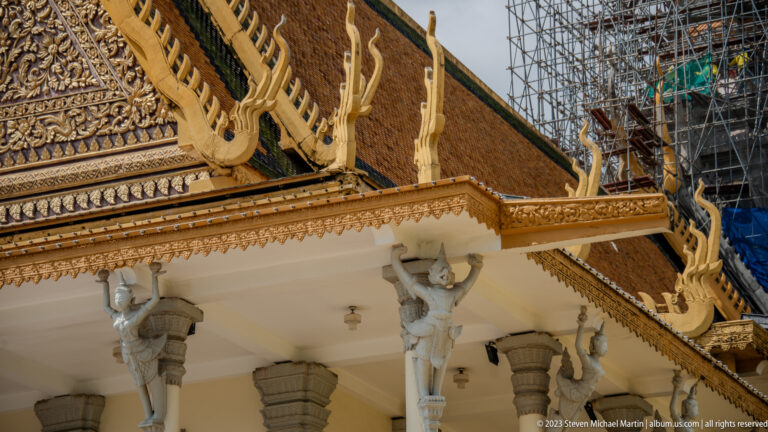 Row of kneeling sculpted figures supporting a palace eave above stone columns and gilded roof ornament.