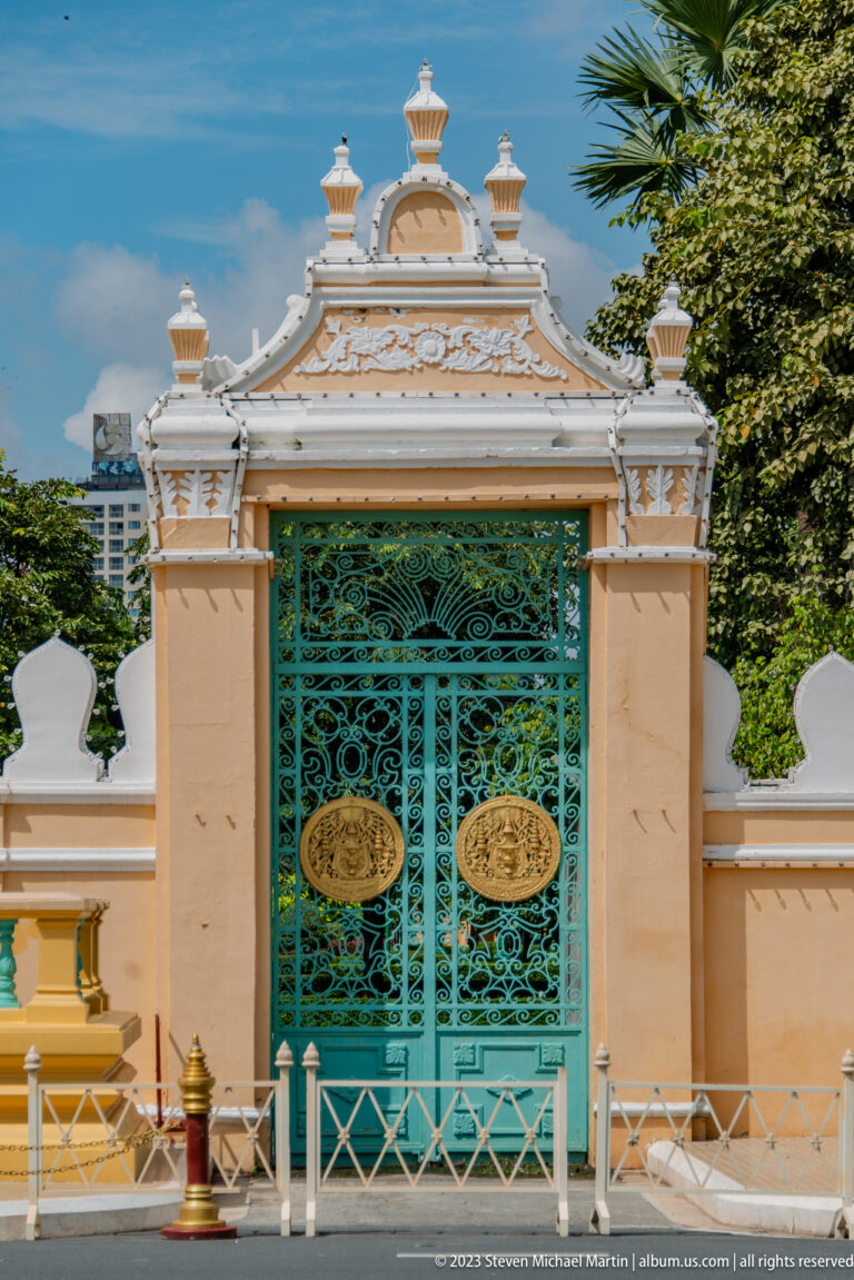 Turquoise ornamental metal gate with gilded medallions set in a peach and white palace wall.