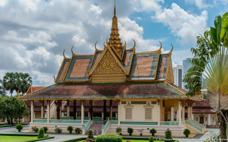 Open palace pavilion with deep eaves, ornate central pediment, turquoise railings, cream walls, and broad stairs.