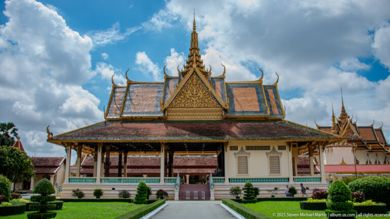 Centered open palace pavilion with colonnade, gilded gable, dark interior, turquoise railings, and broad central stair.
