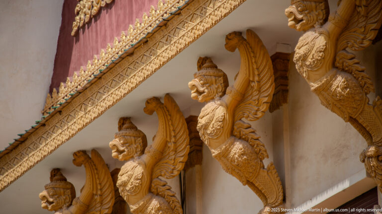 Row of gilded winged garuda figures projecting beneath a richly decorated palace roof edge.