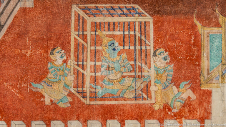 Reamker mural with a costumed figure inside a barred enclosure and attendants on both sides.