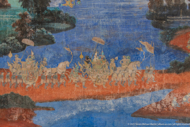 Reamker mural with a long procession of mounted figures, attendants, parasols, and weapons across red and blue ground.