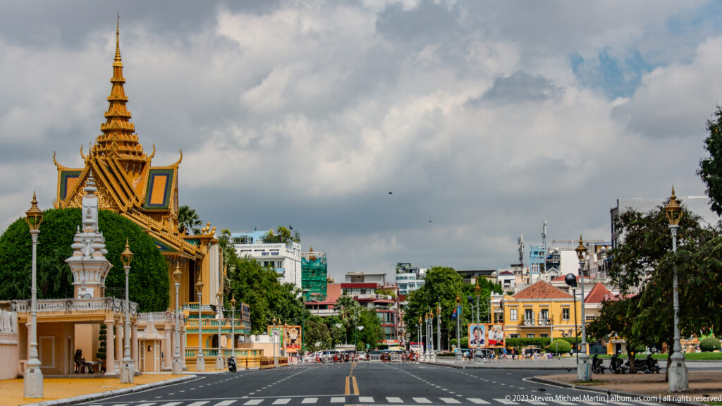 Oblique boulevard view of Royal Palace walls, gates, gilded roofs, trees, and city buildings in Phnom Penh.