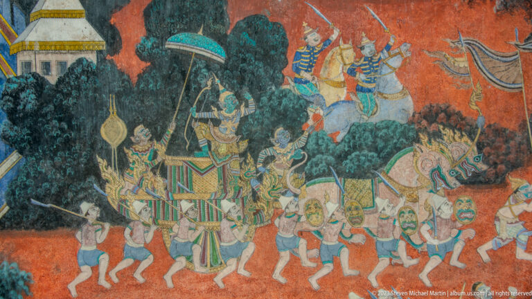 Reamker mural battle scene with armed figures, raised weapons, and a decorated central chariot or platform.