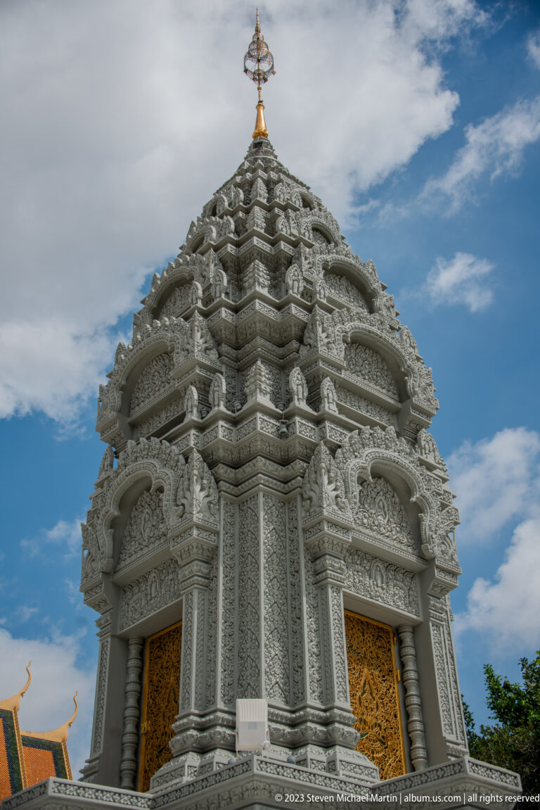 Low-angle close view of a white carved stupa with layered cornices, niches, columns, and gilded doors.