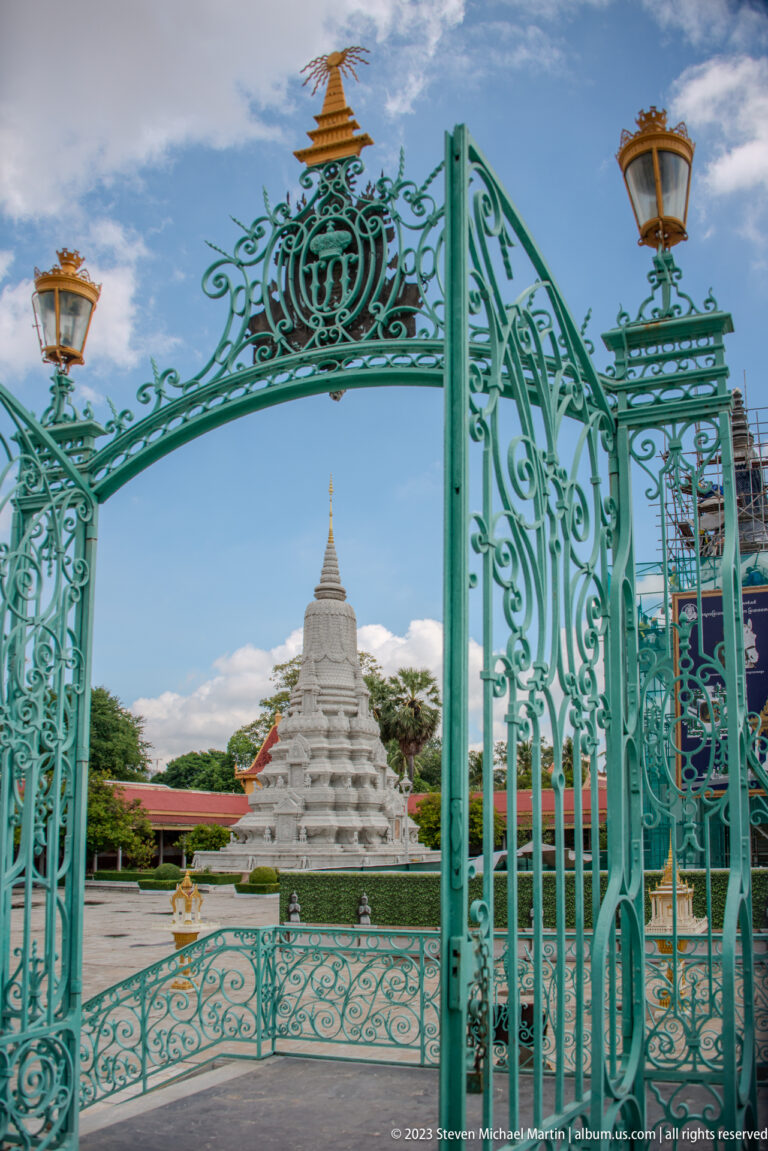 Open turquoise ornamental gate with scrollwork and lanterns framing a distant white stupa.