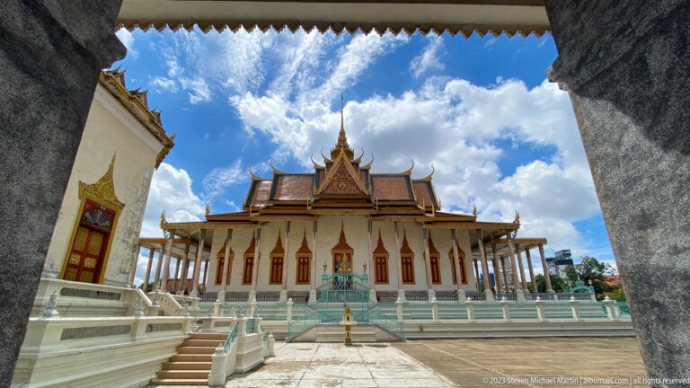 Silver Pagoda framed through a dark opening across a bright courtyard, with white columns, turquoise stairs, and ornate roof.