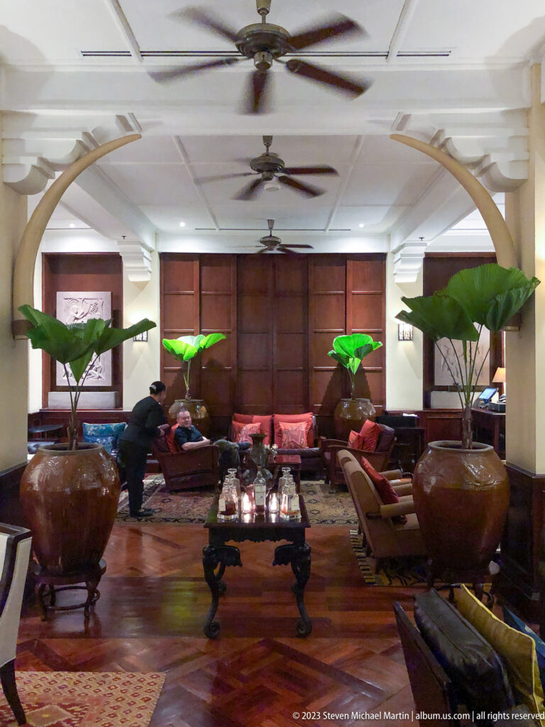 Symmetrical hotel lounge with ceiling fans, curved arches, large planters, sofas, and a candlelit central table.