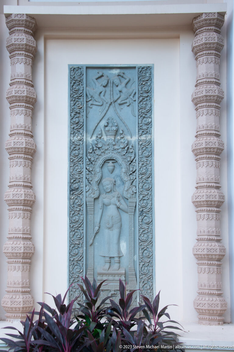 Blue-gray relief of a dancing female figure in a recessed panel between elaborately carved pale columns.