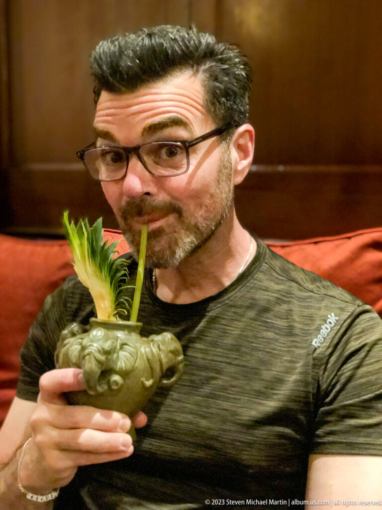 Man sipping through a straw from an elephant-shaped cocktail vessel with pineapple garnish.