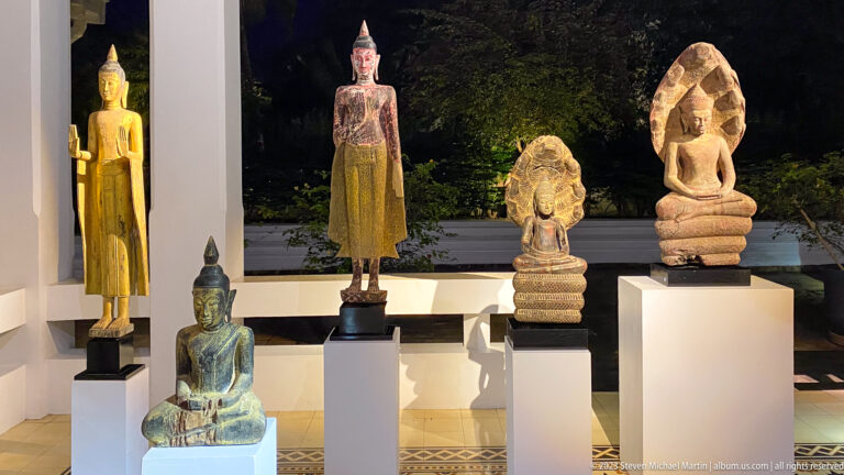 Standing and seated Buddha figures with two naga-protected sculptures displayed on white plinths.