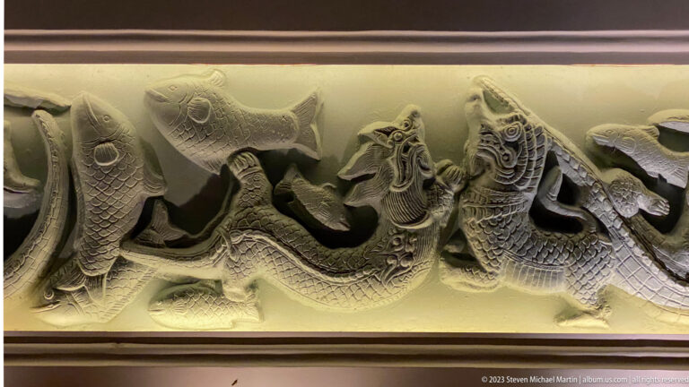 Close detail of carved fish-scaled, dragon-like creatures twisting through an illuminated frieze.