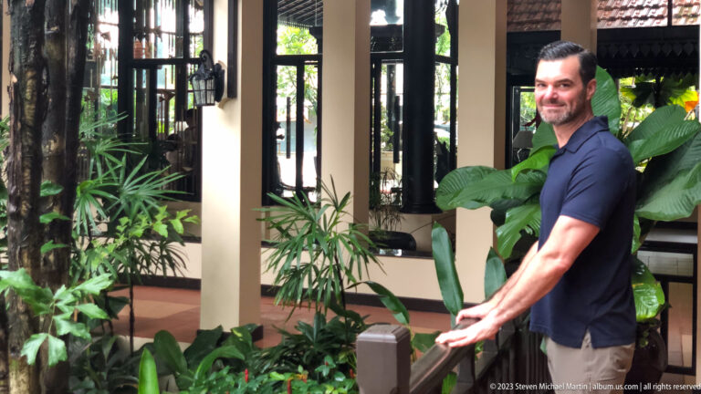 Man standing beside tropical plants in hotel.