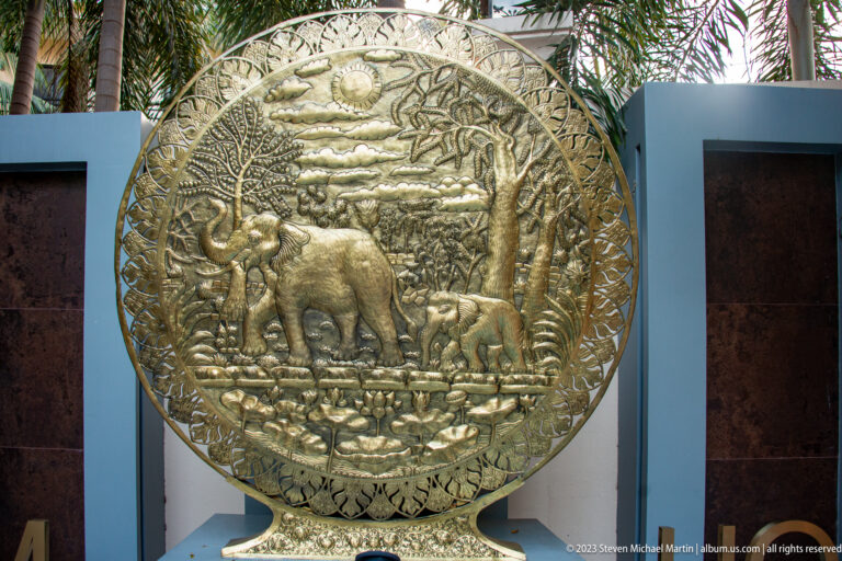Close view of a round metallic-toned relief with elephants, birds, foliage, and a decorative border.