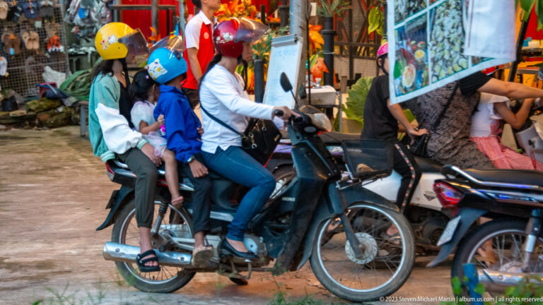 Adult rider carrying several children on a motorbike, photographed in motion on a Siem Reap street.