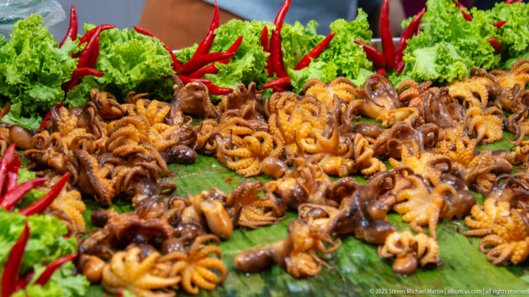 Cooked baby octopuses glazed with sauce and arranged on banana leaves with red chilies and curly lettuce.