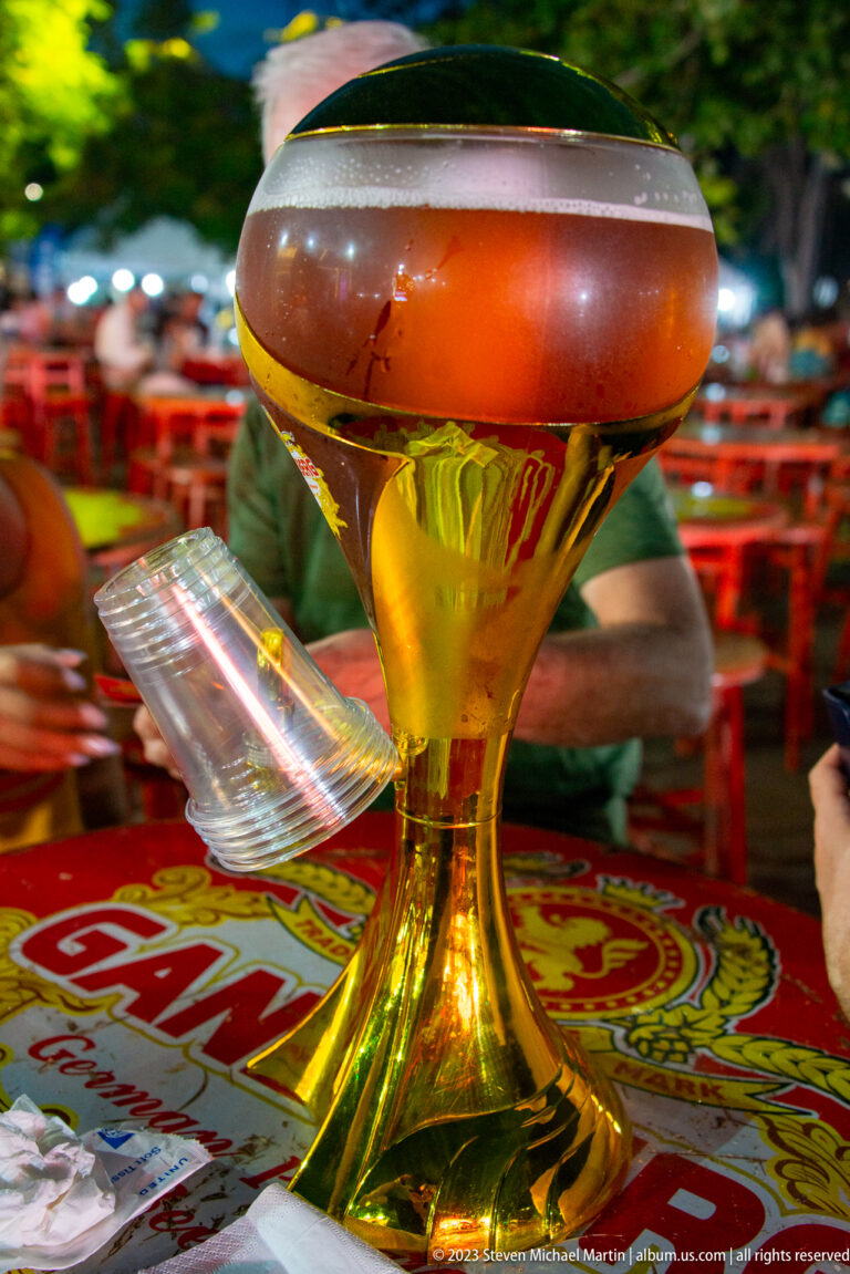 Translucent amber-and-white bowl on a gold pedestal beside plastic utensils on a Ganzberg-branded table.
