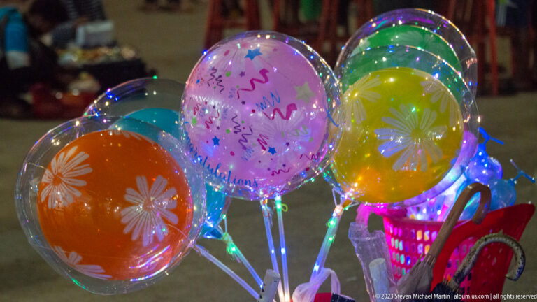 Cluster of transparent LED balloons containing colored inner balloons and printed decorations at a night market.