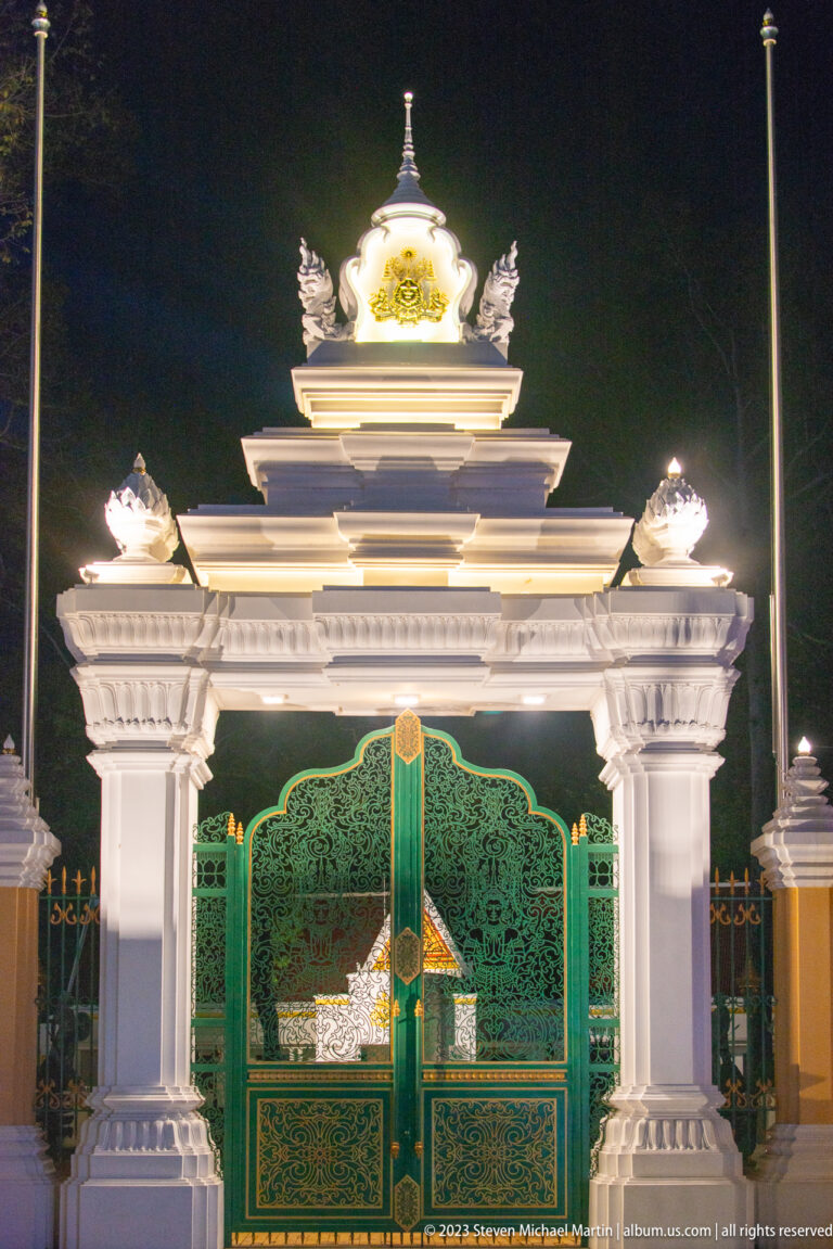 Frontal view of ornate green metal doors beneath a white illuminated gateway with tiered lintels and gilded details.