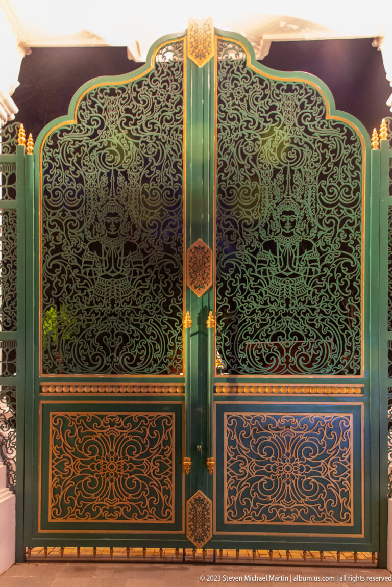 Close view of green ornamental metal gates with animal figures, scrolling foliage, and gold-blue lower panels.