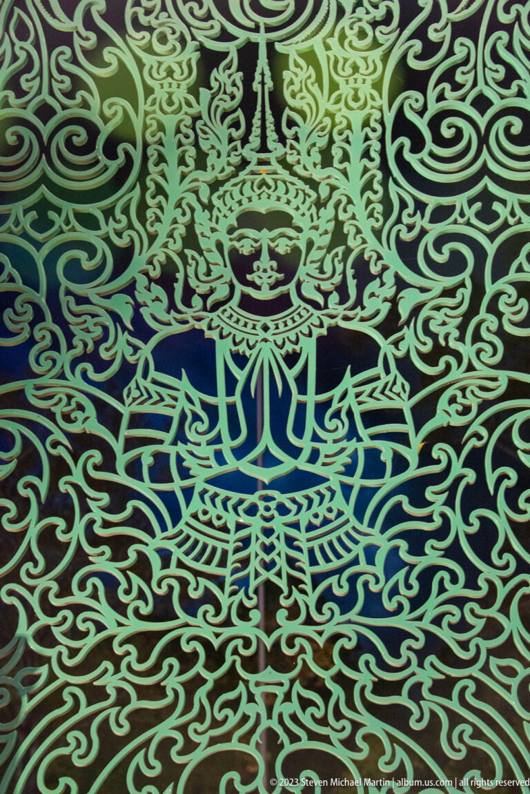 Close detail of a crowned stylized figure surrounded by curling green metal patterns.