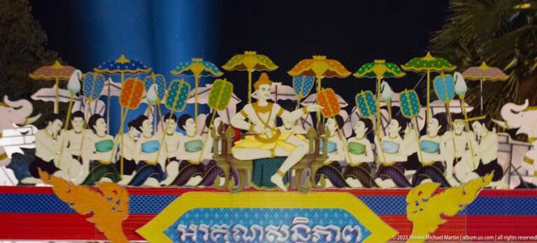 Colorful mural of a central ceremonial figure surrounded by attendants holding parasols above Khmer text.