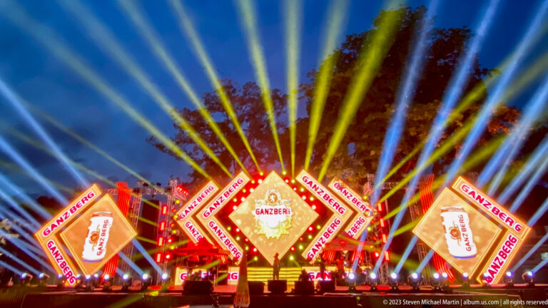 Bright Ganzberg stage with yellow and blue beams radiating upward at night.