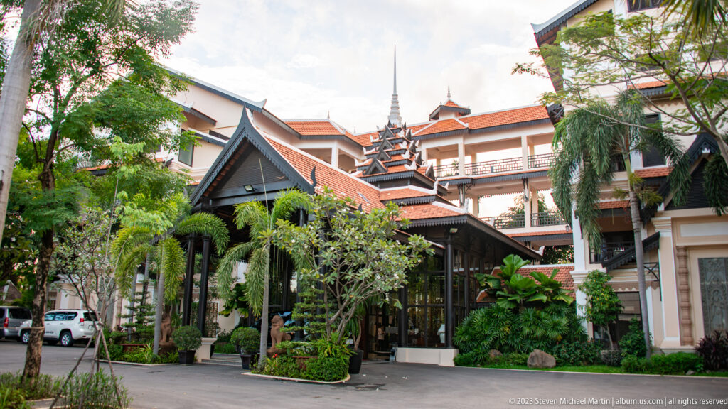 Hotel entrance with steep layered gables, red tile roofs, timber details, verandas, and tropical landscaping.