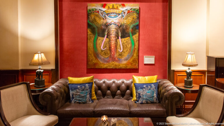 Colorful elephant painting above a dark leather sofa with yellow cushions and matching table lamps.