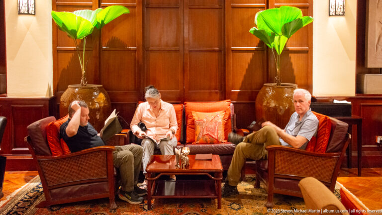 Three adults seated in rattan chairs around a small table in a wood-paneled hotel lounge.
