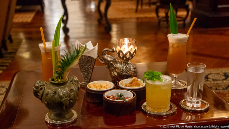 Assorted cocktails, iced drinks, snacks, and a pineapple-shaped vessel arranged on a polished table.