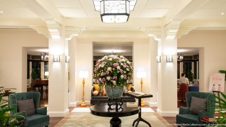 Large pink-and-white floral arrangement centered in a bright hotel lobby with white columns and seating.
