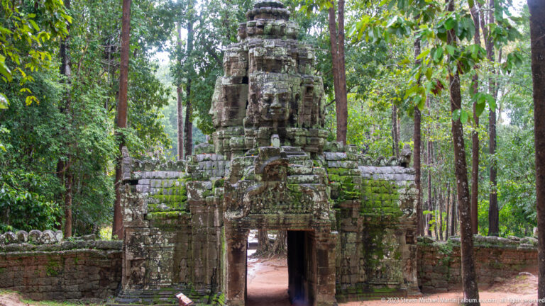 Moss-covered Ta Som entrance tower with a large carved face above a central doorway in dense forest.